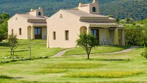 A two-story building with a tiled roof and arched windows, surrounded by a grassy landscape and a hill in the background. - Family Rooms Budoni (Budoni)