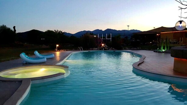 A swimming pool with hot tubs and a jacuzzi, surrounded by a landscaped area with a view of mountains. - Family Rooms Budoni (Budoni)