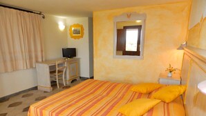 A hotel room with a bed, a desk, a television, and a small bedside table with a vase of flowers. - Family Rooms Budoni (Budoni)
