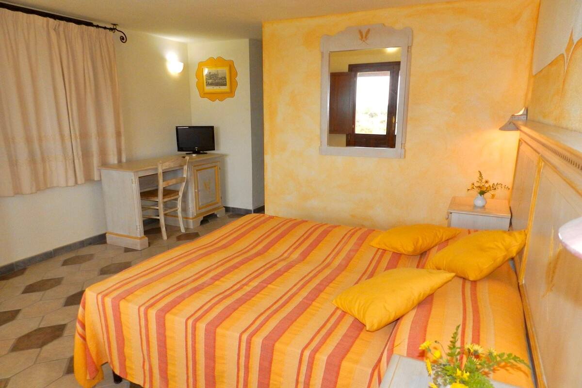Une chambre d’hôtel équipée d’un lit, d’un bureau, d’une télévision et d’une petite table de chevet agrémentée d’un vase de fleurs.