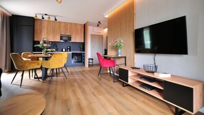 Una sala de estar moderna con piso de madera, un área de comedor con sillas amarillas, una cocina con microondas y un televisor de pantalla plana montado en la pared.