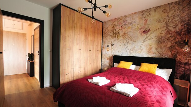 Une chambre avec une grande armoire en bois, un lit avec une literie rouge et un papier peint à motifs floraux.