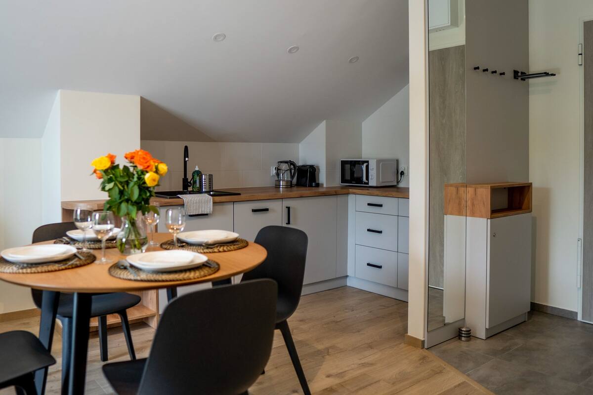 Una cocina moderna con comedor, con una mesa de madera dispuesta para cuatro, un florero con flores y un microondas en la encimera.