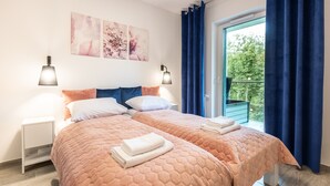 Una cama doble con colcha naranja acolchada, dos mesitas de noche con lámparas y una ventana con cortinas azules.