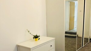 A white dresser with three drawers and a small plant on top, positioned next to a white closet with a mirrored door.