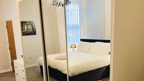 A bedroom with a large mirror, a bed, a dresser, and a window with blinds.