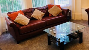 A living room with a brown leather sofa, a glass coffee table, and large windows with blinds.