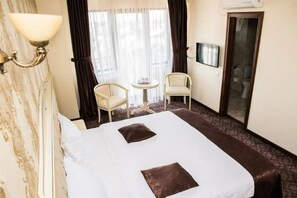 Una habitación de hotel con una cama grande, dos sillas, una mesita y un televisor.