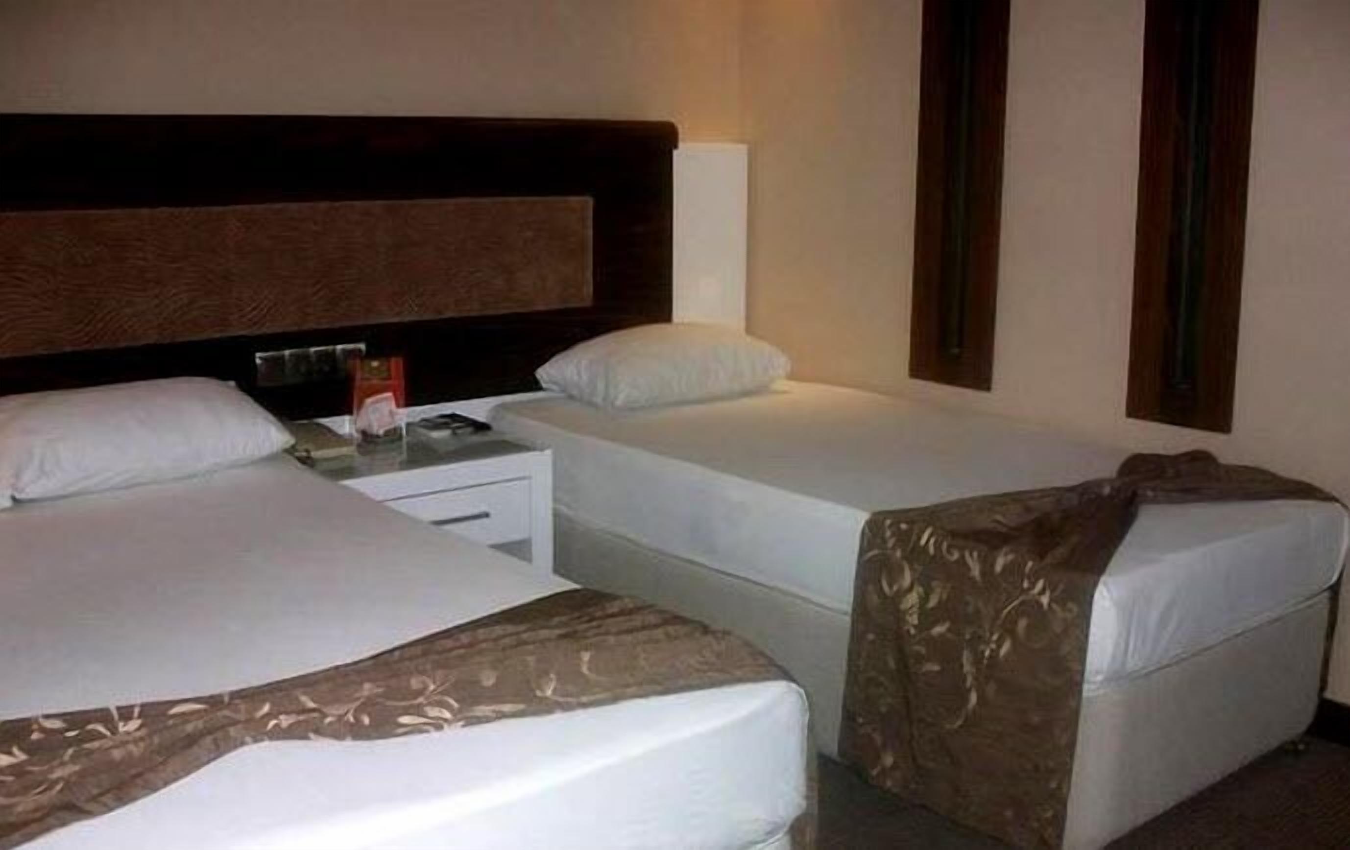 A hotel room with two single beds, a nightstand, a lamp, and a wall-mounted TV.