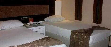 A hotel room with two single beds, a nightstand, a lamp, and a wall-mounted TV.