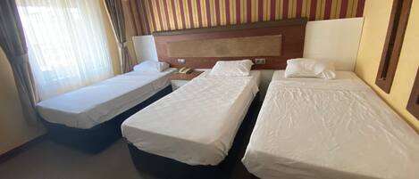 A hotel room with two single beds, a wooden headboard, a telephone, and a window with curtains.