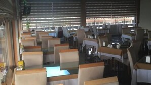 A restaurant with booths and tables, large windows, and a view of buildings outside. - Mostar Hotel (Antalya)
