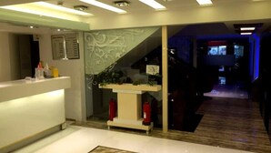 A modern reception area with a white counter, decorative wall panel, and a staircase leading to a lower level. - Mostar Hotel (Antalya)