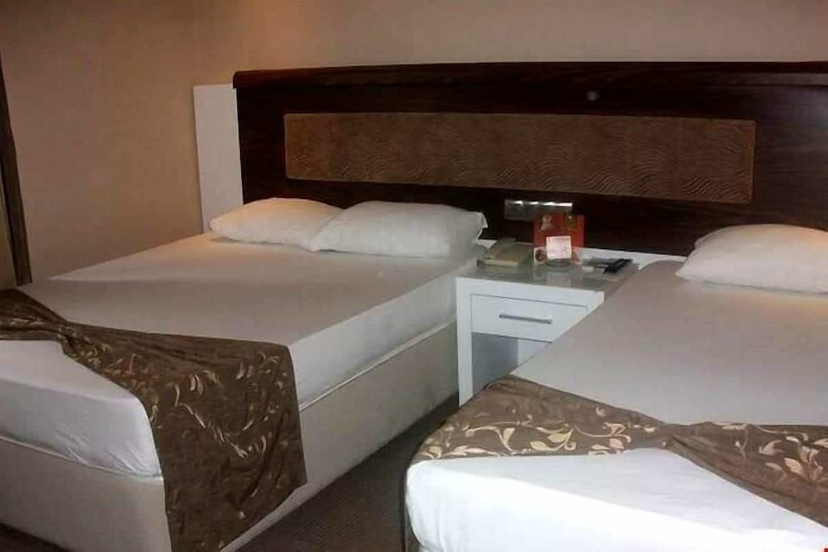 A hotel room with two beds, each with white linens and a brown patterned bedspread. There is a small bedside table with a lamp and a phone.