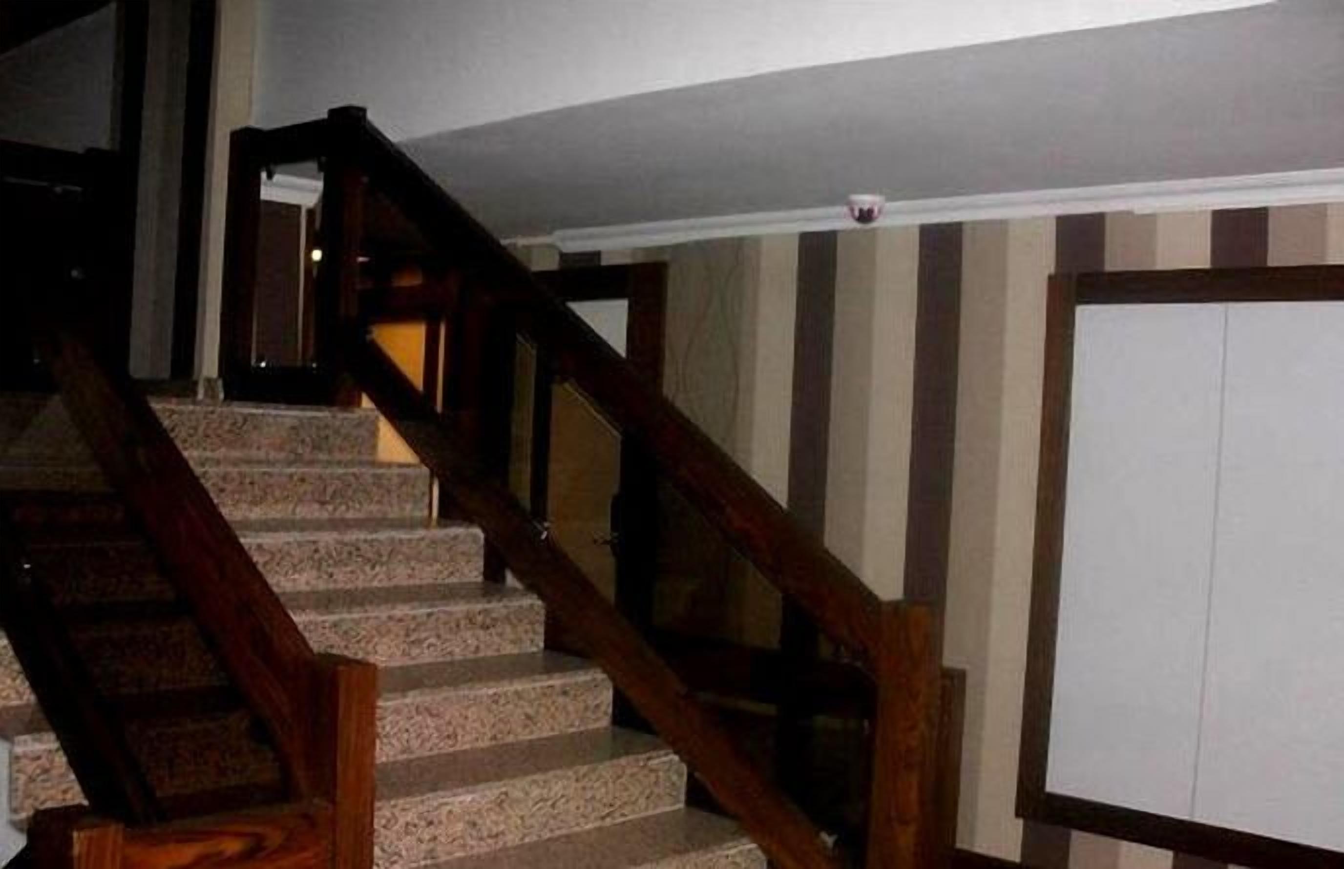 A staircase with wooden handrails and stone steps, leading to a door with a striped wall in the background.