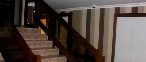 A staircase with wooden handrails and stone steps, leading to a door with a striped wall in the background.
