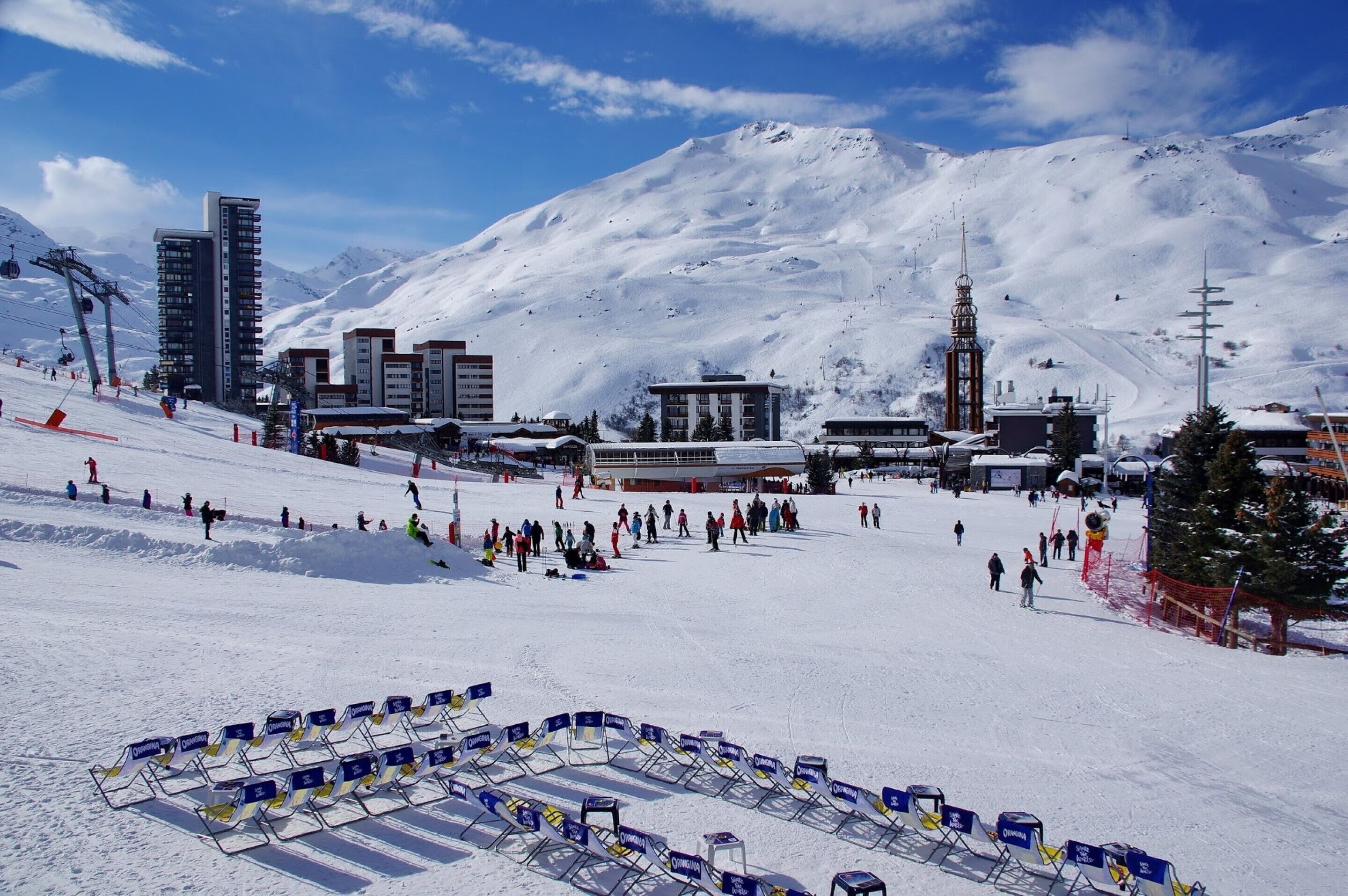 A snowy ski resort with a ski lift, buildings, and a mountain in the background.