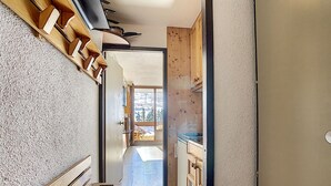 A narrow hallway with wooden benches and cabinets, leading to a balcony with a view of trees and a snowy landscape.