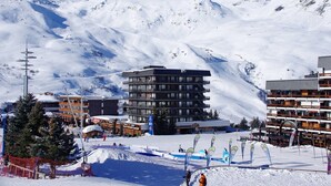 A modern ski resort with multi-story buildings, ski lifts, and a snowy mountain backdrop.