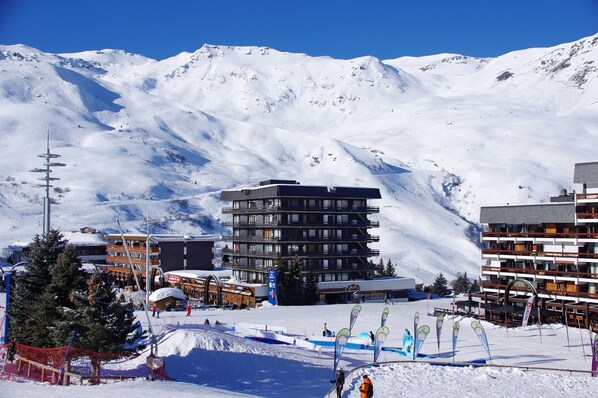 Un moderno complejo de esquí con edificios de varios pisos, telesillas y una montaña nevada al fondo.
