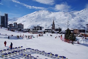 Estación de esquí con pistas nevadas, edificios y montañas al fondo.