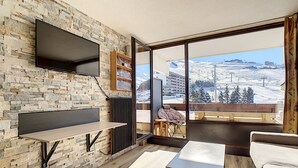 A modern living room with a stone wall, a flat-screen TV, a fireplace, and a large window offering a snowy mountain view.
