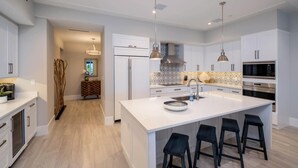 Une cuisine moderne avec des meubles blancs, des appareils en acier inoxydable et un îlot central doté de tabourets de bar.