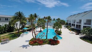 Un complexe hôtelier doté d’une piscine entourée de palmiers et d’un bâtiment blanc agrémenté de balcons.