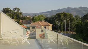 A modern building with a glass balcony overlooking a parking area and a view of houses and mountains.
