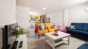 A modern living room with a white coffee table, a blue sofa, and a yellow armchair. A kitchen with yellow cabinets and a refrigerator is visible in the background. - Dromroe Village University of Limerick (Limerick)