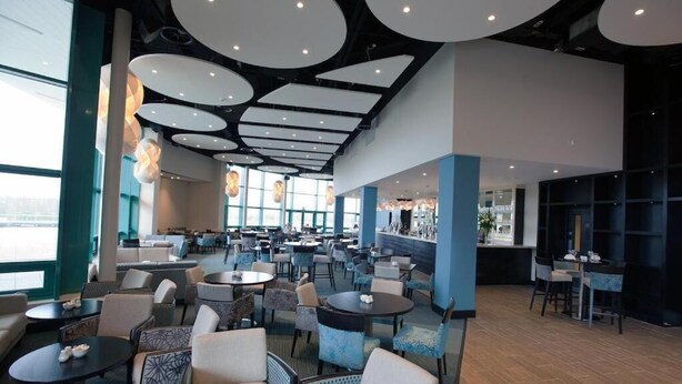 A spacious indoor area with multiple seating arrangements, including round tables and chairs, and a bar area with a counter. - Dromroe Village University of Limerick (Limerick)