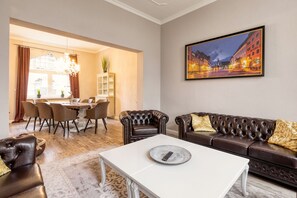 A living room with a white coffee table, a brown leather sofa, and a dining area with a chandelier. - Exclusive Villa an der Bode (Thale)