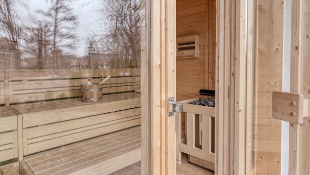 Un sauna en bois doté d’une porte en verre, d’un banc en bois et d’un appareil de chauffage pour sauna visible à travers la porte.