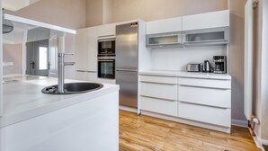 Une cuisine moderne avec des meubles blancs, un réfrigérateur en acier inoxydable et un four encastré.