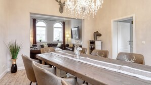 Un coin repas avec une table en bois, des chaises, un lustre et un téléviseur en arrière-plan.
