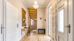 Un couloir doté d’un parquet en bois, de portes blanches, d’un lustre et d’un escalier avec une rampe dorée.