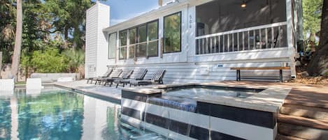 Una casa moderna con piscina, mobiliario exterior y un porche cubierto.