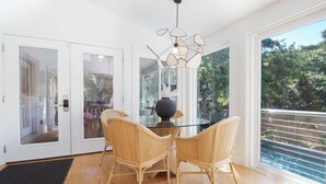Un comedor con una mesa de vidrio y sillas de mimbre, una lámpara moderna y vistas al verdor exterior.