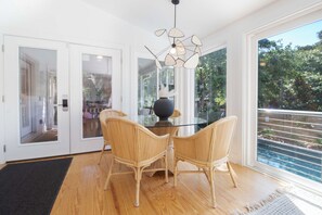 Un comedor con una mesa de vidrio y sillas de mimbre, una lámpara moderna y vistas al verdor exterior.