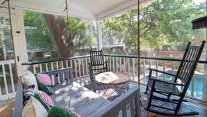A covered outdoor seating area with a table and chairs, a swing, and a view of a swimming pool. - Newly Renovated 1 Block from Beach w/Pool!~The Jolly Folly (Folly Beach)