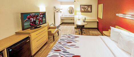 Une chambre d’hôtel avec un lit, une télévision, un bureau, une chaise, une petite table et une salle de bain à l’arrière-plan.