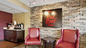 A Red Roof Inn reception area with a stone wall, two leather chairs, a small table, and a coffee station.