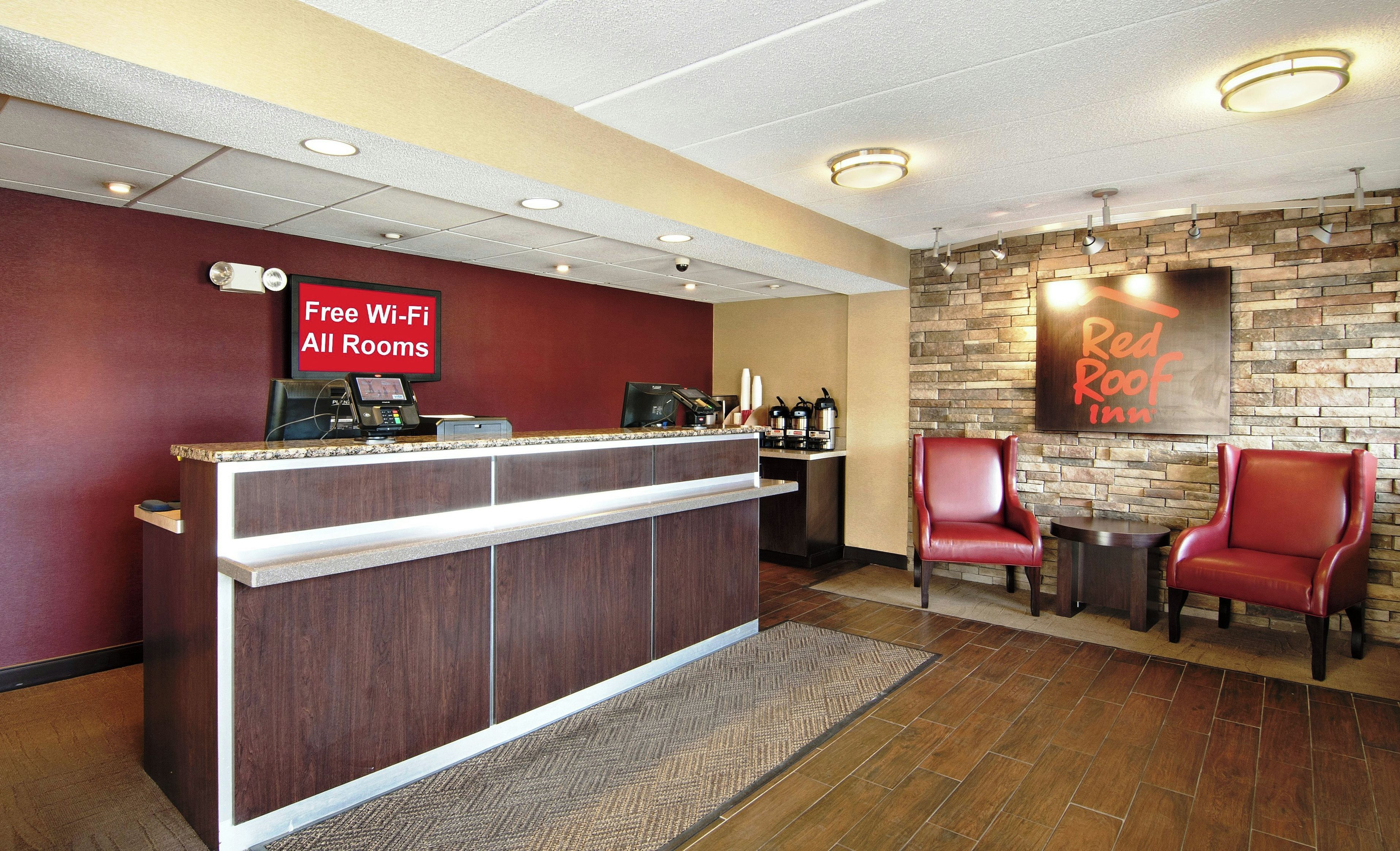 A reception area with a counter, a coffee station, and two red chairs.