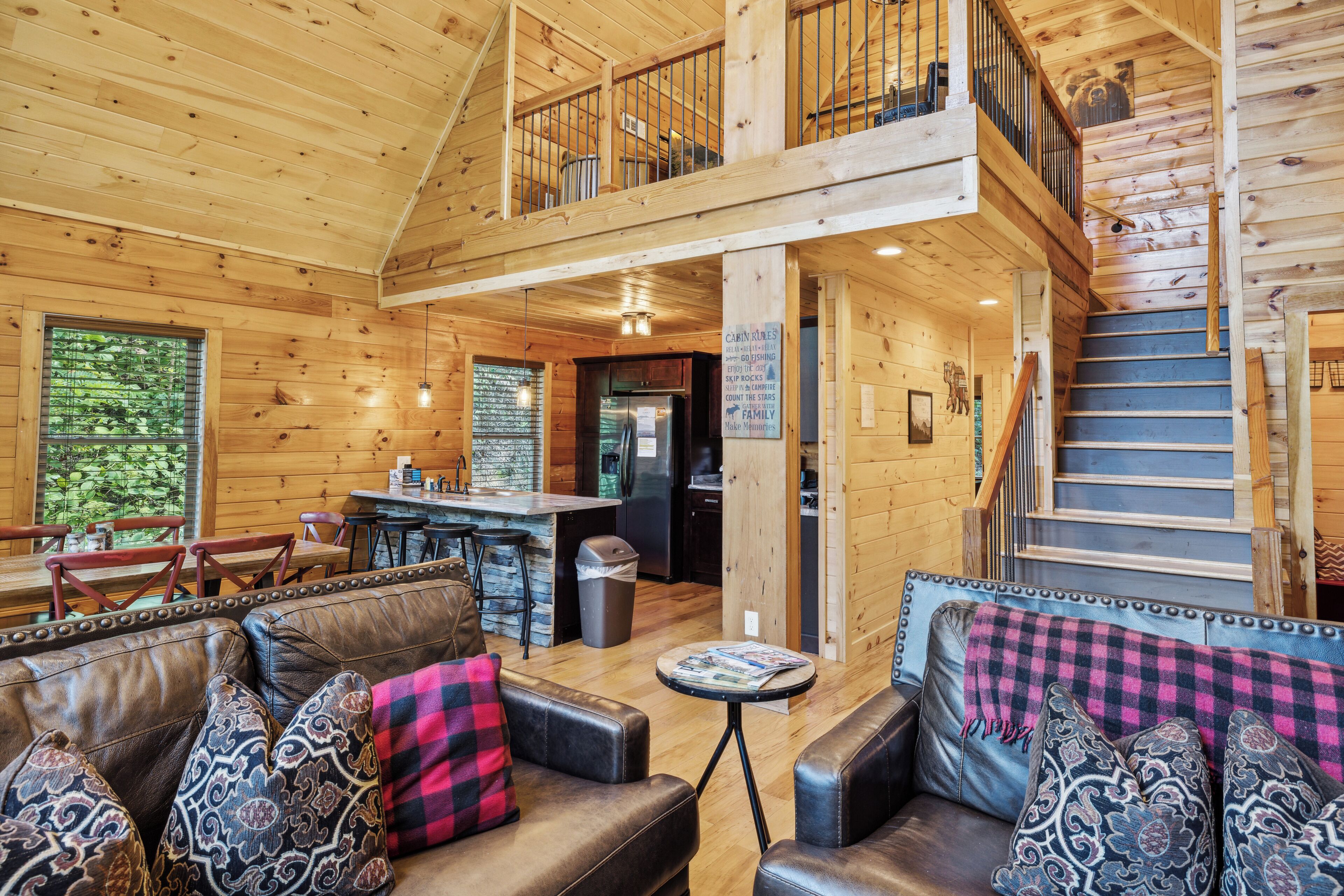 A spacious cabin interior with a dining area, kitchen, and a staircase leading to a loft.
