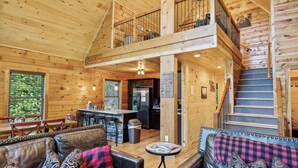 A spacious cabin interior with a dining area, kitchen, and a staircase leading to a loft.