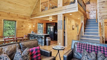 A spacious cabin interior with a dining area, kitchen, and a staircase leading to a loft.