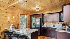 A kitchen with wooden walls, a marble island, and a stainless steel refrigerator.