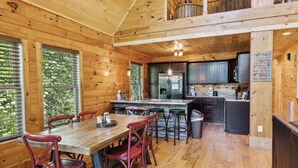 A wooden cabin interior with a dining area, kitchen, and a balcony.