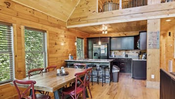 A wooden cabin interior with a dining area, kitchen, and a balcony.