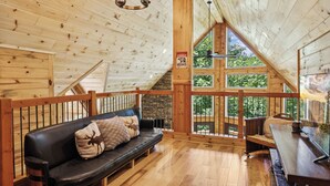 A wooden cabin interior with a black leather sofa, a wooden dining table, and a stone fireplace.